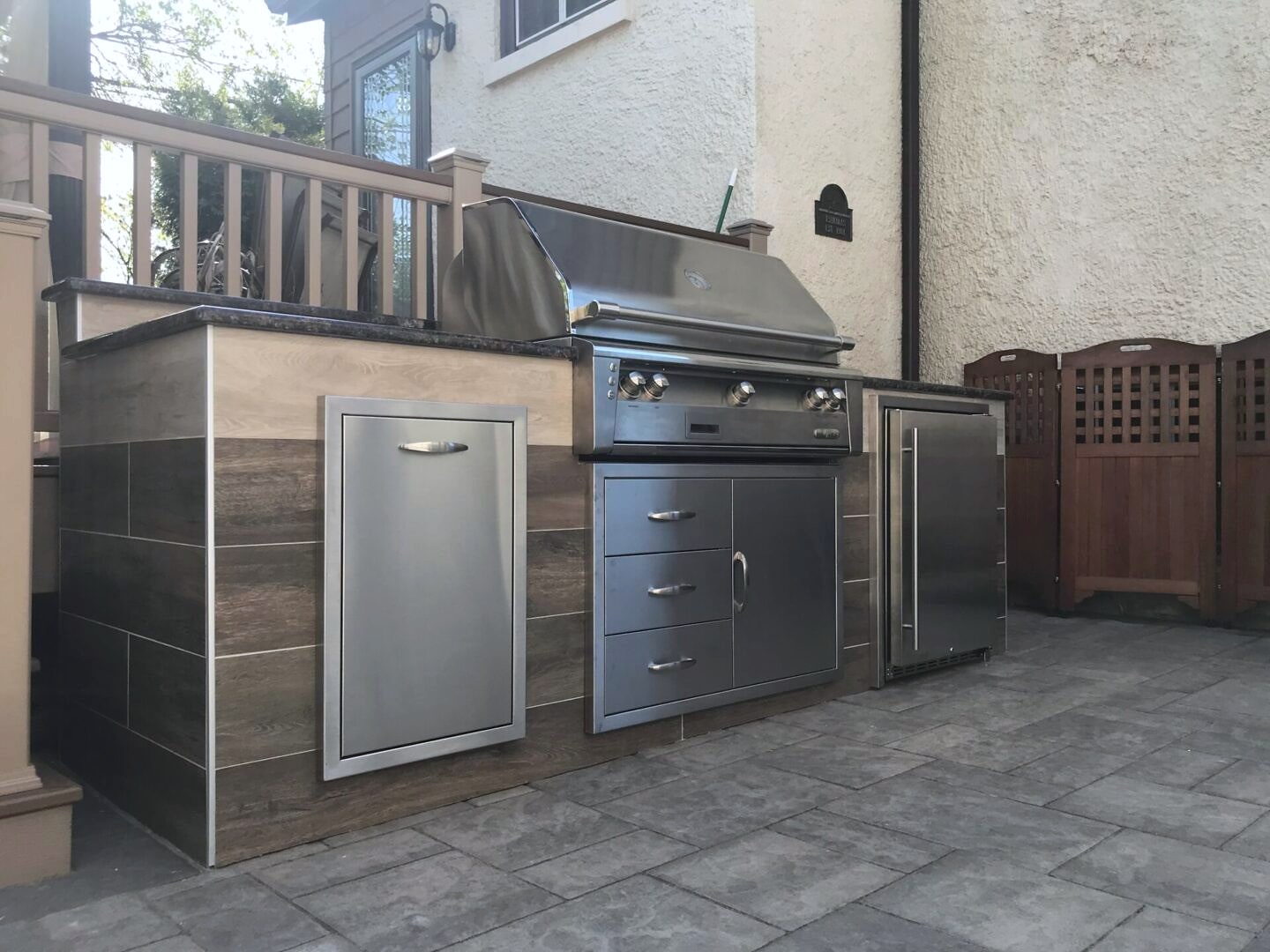 Outdoor kitchen with stainless grill and fridge on paver patio