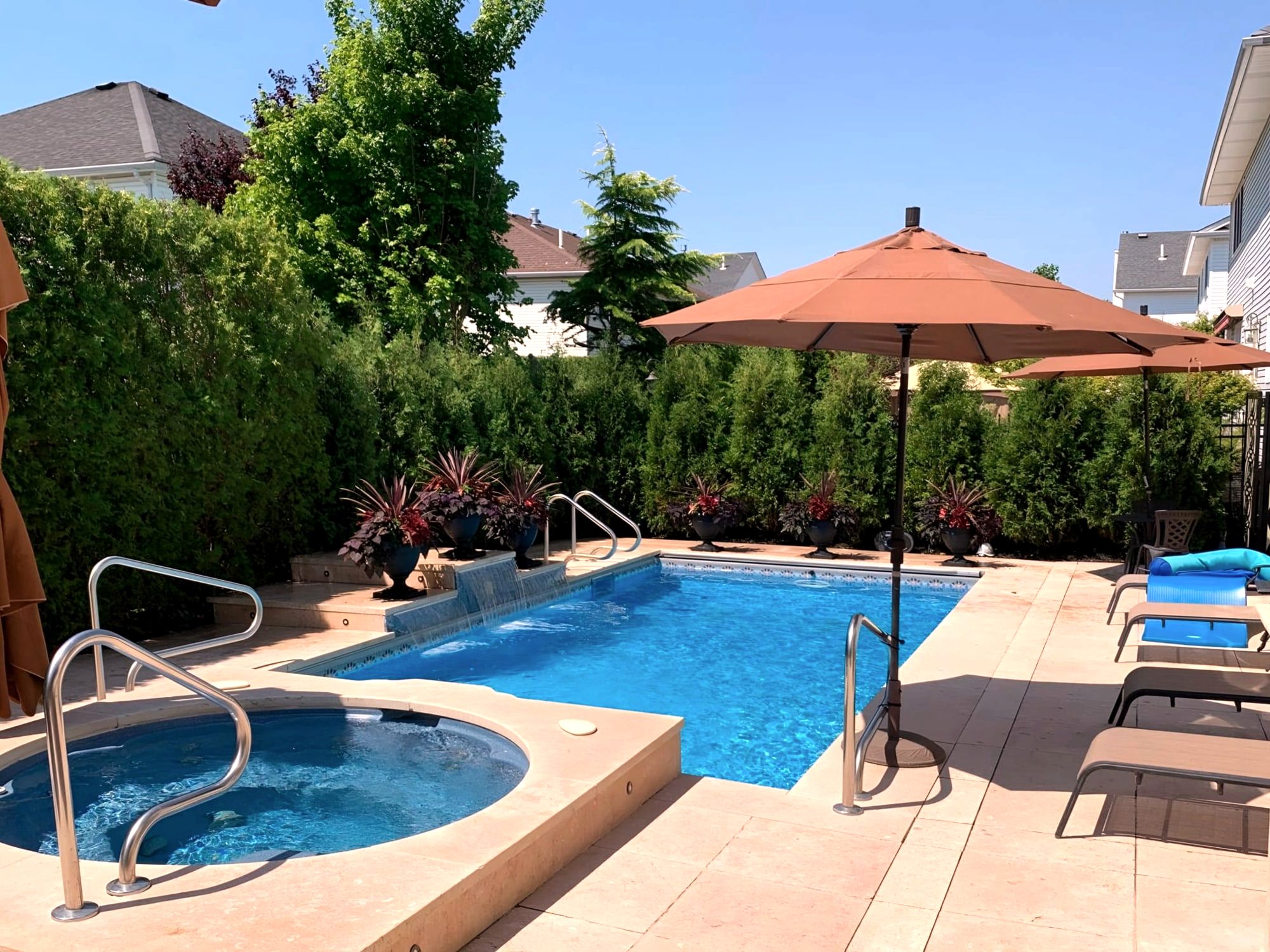 Backyard pool and hot tub with paver deck, umbrellas, hedges